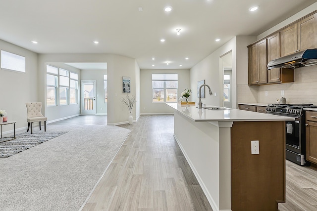 kitchen featuring a center island with sink, light hardwood / wood-style flooring, gas stove, sink, and tasteful backsplash