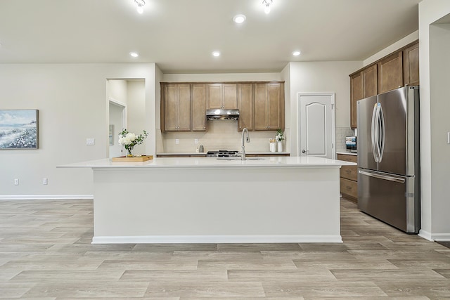 kitchen with stainless steel refrigerator, light hardwood / wood-style floors, a center island with sink, and sink