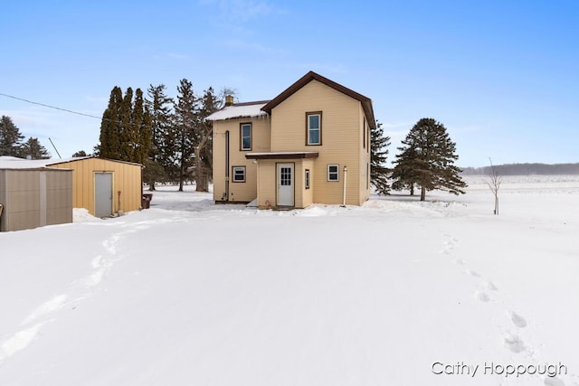 snow covered rear of property with a storage unit