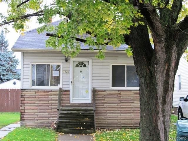 view of front of house with entry steps, stone siding, fence, and roof with shingles