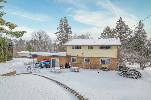 snow covered property with a patio area, brick siding, and a chimney