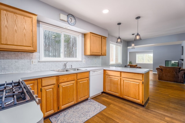 kitchen with decorative backsplash, dark wood-style flooring, a peninsula, white dishwasher, and a sink