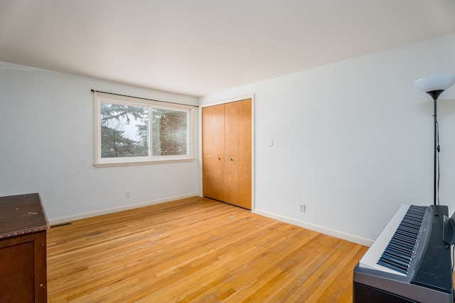 unfurnished bedroom with a closet, light wood-style flooring, baseboards, and heating unit