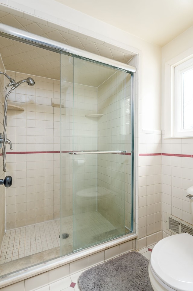 bathroom with a shower stall, toilet, and tile walls