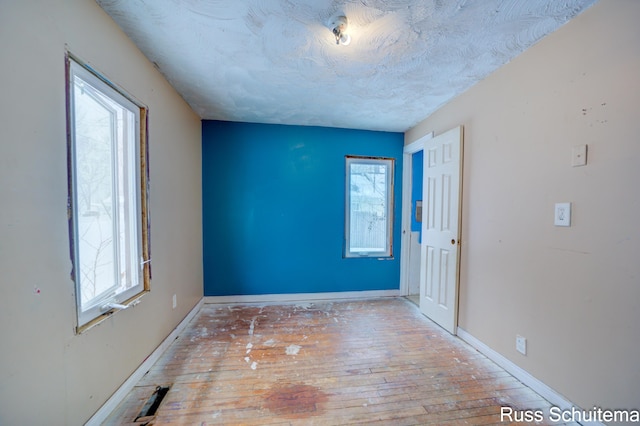 empty room featuring a wealth of natural light, a textured ceiling, and hardwood / wood-style flooring