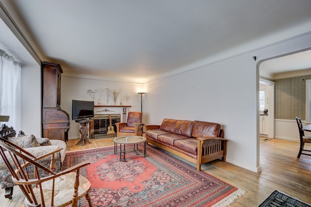 living area with light wood-style floors, baseboards, arched walkways, and a glass covered fireplace