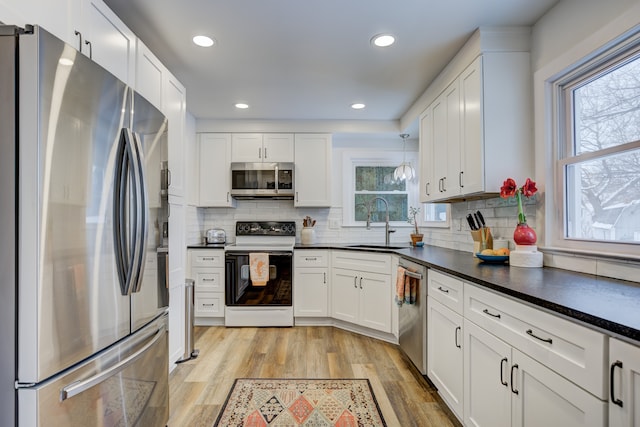 kitchen featuring stainless steel appliances, white cabinets, a sink, and light wood-style flooring