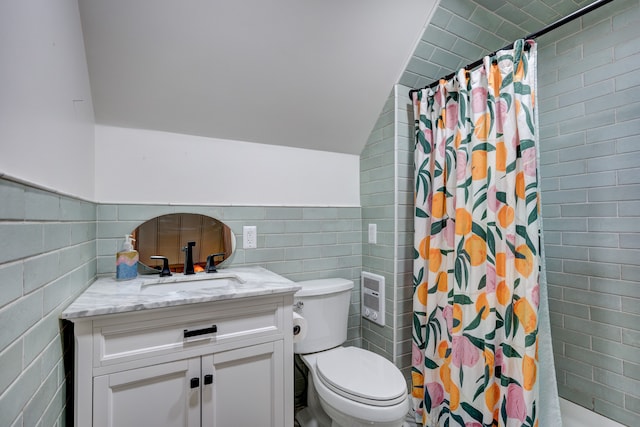 full bath with tile walls, toilet, vaulted ceiling, vanity, and tiled shower