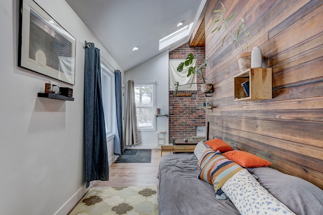 bedroom featuring vaulted ceiling with skylight, wood walls, baseboards, and recessed lighting