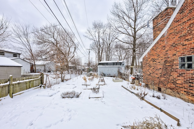 yard layered in snow with a storage shed, an outdoor structure, fence, and a garage