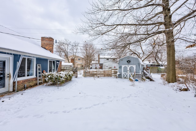 snowy yard with an outbuilding, a storage shed, and fence