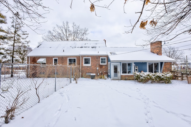 snow covered back of property featuring central AC, brick siding, fence, and a chimney