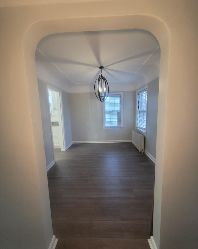 unfurnished room featuring dark hardwood / wood-style floors, a chandelier, and radiator heating unit