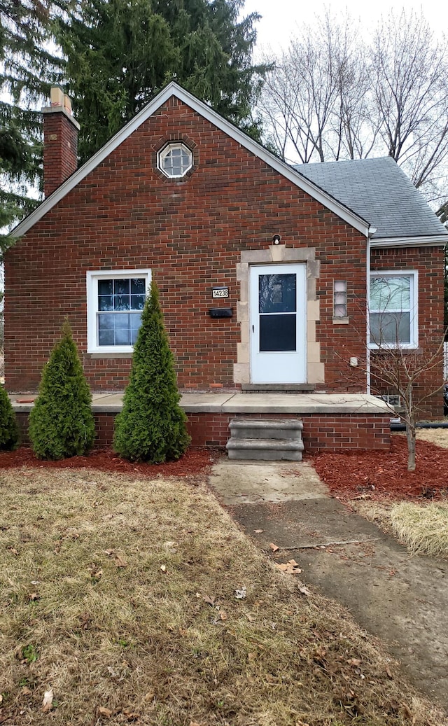 view of front of house with brick siding, a chimney, and roof with shingles