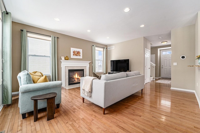 living room with light hardwood / wood-style floors, a wealth of natural light, and a high end fireplace