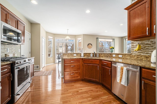 kitchen with appliances with stainless steel finishes, sink, light stone counters, decorative light fixtures, and light hardwood / wood-style floors