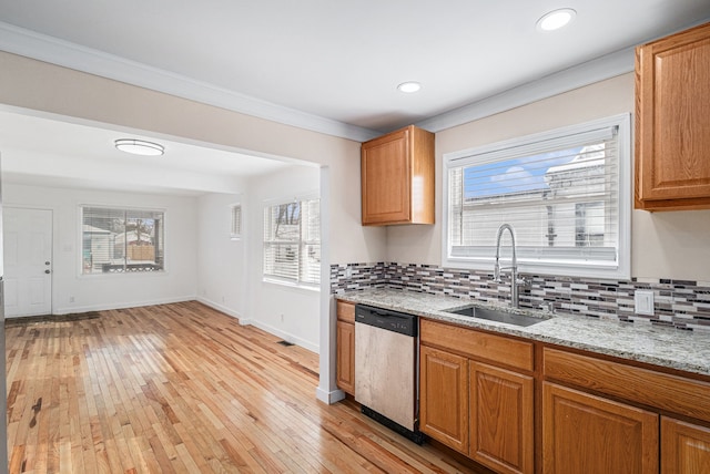 kitchen with dishwasher, light wood-style flooring, backsplash, light stone countertops, and a sink