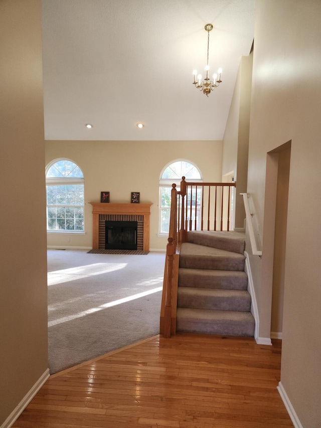 stairway featuring a brick fireplace, hardwood / wood-style floors, a notable chandelier, and a wealth of natural light