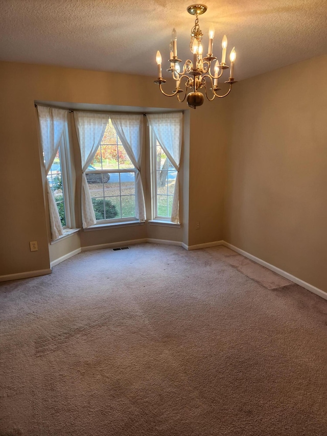 carpeted empty room featuring a chandelier and a textured ceiling