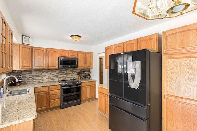 kitchen featuring light wood-type flooring, sink, tasteful backsplash, light stone counters, and appliances with stainless steel finishes