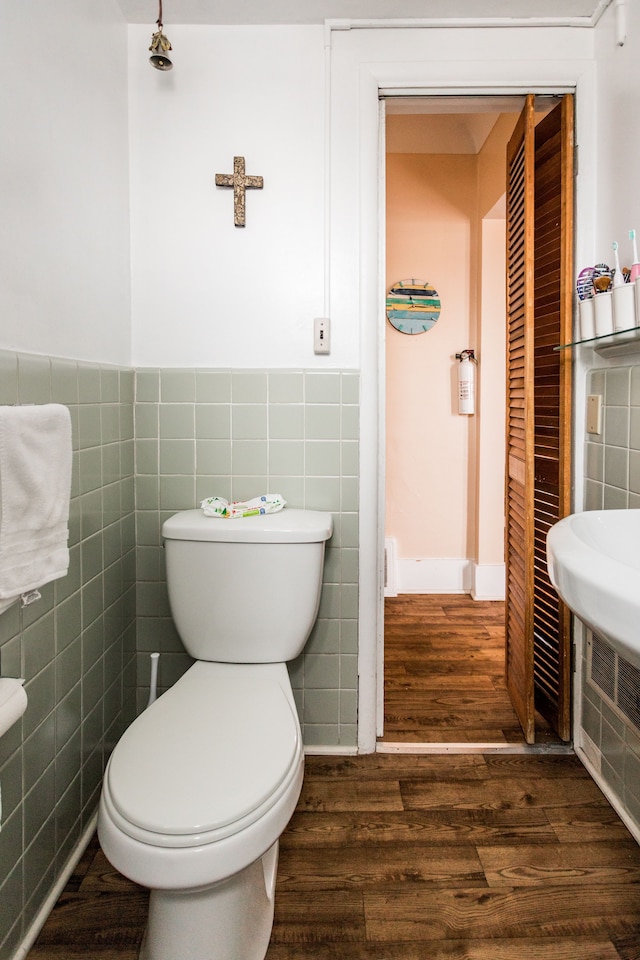 bathroom with toilet, tile walls, wood finished floors, and wainscoting