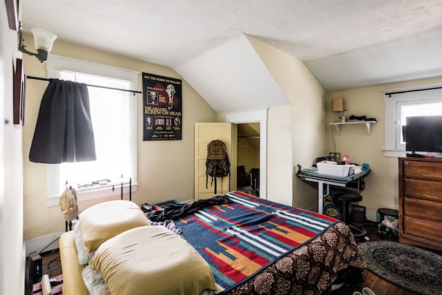 bedroom with multiple windows, vaulted ceiling, and a textured ceiling