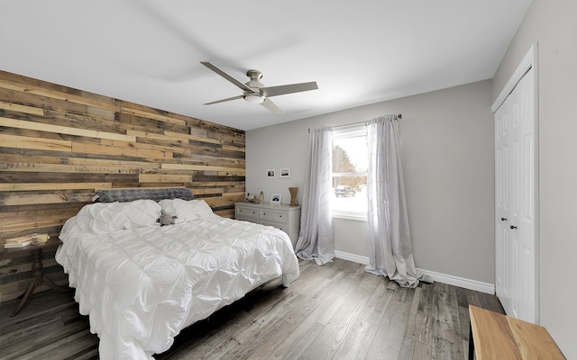 bedroom featuring an accent wall, wood walls, baseboards, a closet, and dark wood-style floors