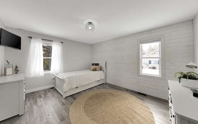 bedroom with baseboards, wood finished floors, visible vents, and wooden walls