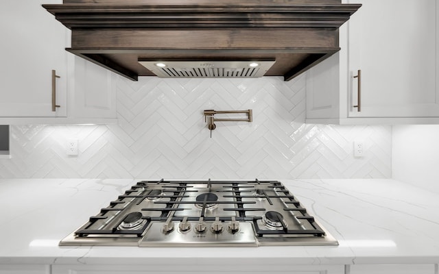 room details with light stone countertops, stainless steel gas cooktop, white cabinets, and decorative backsplash