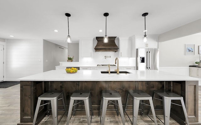 kitchen featuring hanging light fixtures, custom exhaust hood, a kitchen bar, white cabinetry, and high end fridge