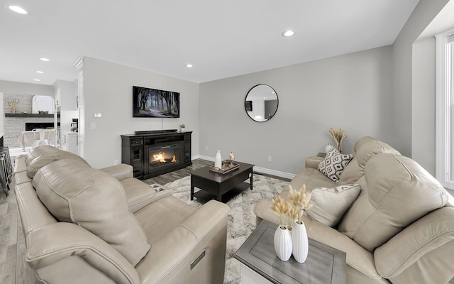 living area featuring a warm lit fireplace, baseboards, and recessed lighting