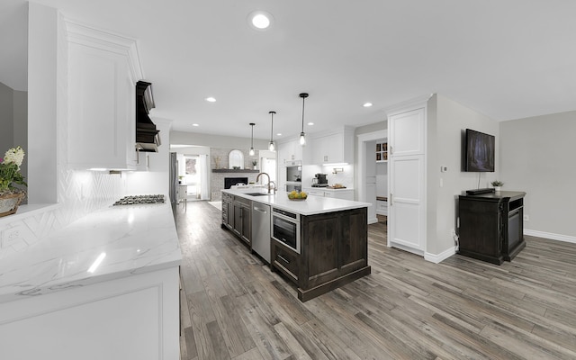 kitchen featuring decorative light fixtures, a sink, white cabinets, light wood-style floors, and a center island with sink