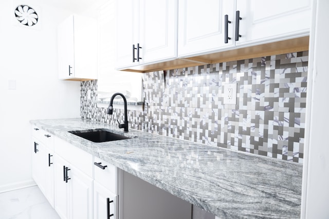 kitchen with backsplash, light stone countertops, white cabinets, marble finish floor, and a sink