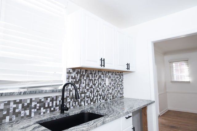 kitchen featuring light stone counters, wood finished floors, a sink, white cabinetry, and backsplash