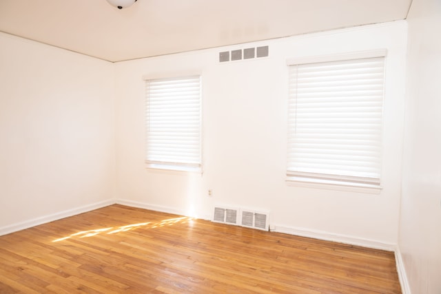 empty room with visible vents, plenty of natural light, baseboards, and wood finished floors