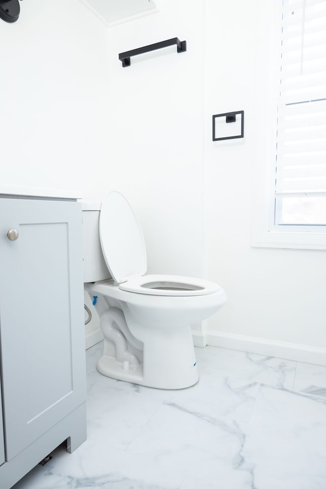 bathroom with marble finish floor, toilet, and baseboards