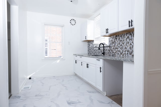 kitchen with marble finish floor, a sink, light stone counters, backsplash, and white cabinetry