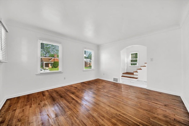 empty room featuring arched walkways, plenty of natural light, stairs, and hardwood / wood-style floors