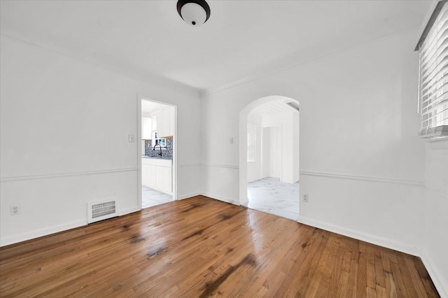 spare room featuring visible vents, arched walkways, baseboards, and hardwood / wood-style floors