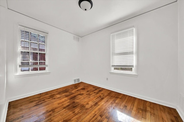 empty room with visible vents, baseboards, and hardwood / wood-style floors