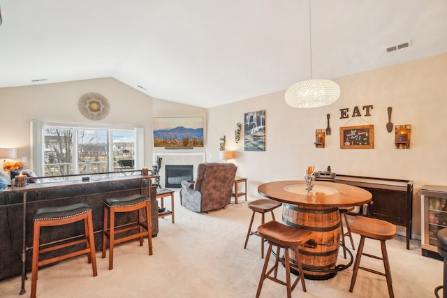 dining room featuring visible vents, a fireplace, vaulted ceiling, wine cooler, and light colored carpet