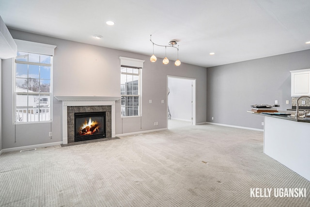 unfurnished living room with light carpet, plenty of natural light, sink, and a fireplace