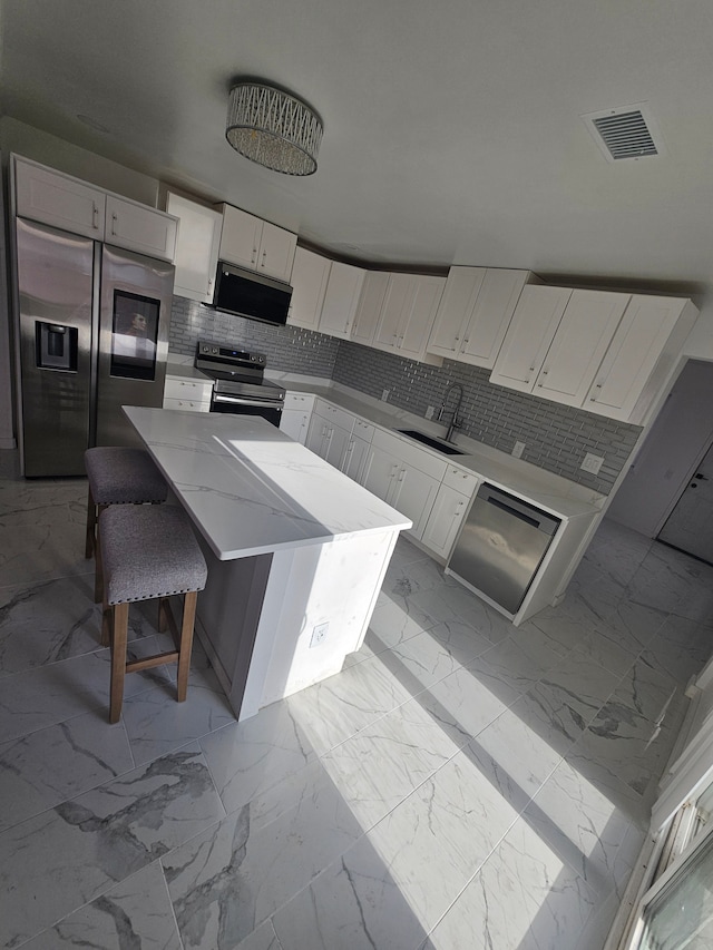 kitchen featuring white cabinetry, a kitchen island, sink, appliances with stainless steel finishes, and a kitchen bar