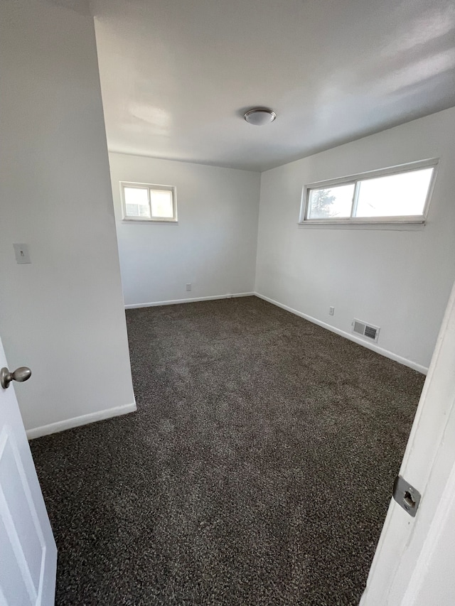 unfurnished room with dark colored carpet and plenty of natural light