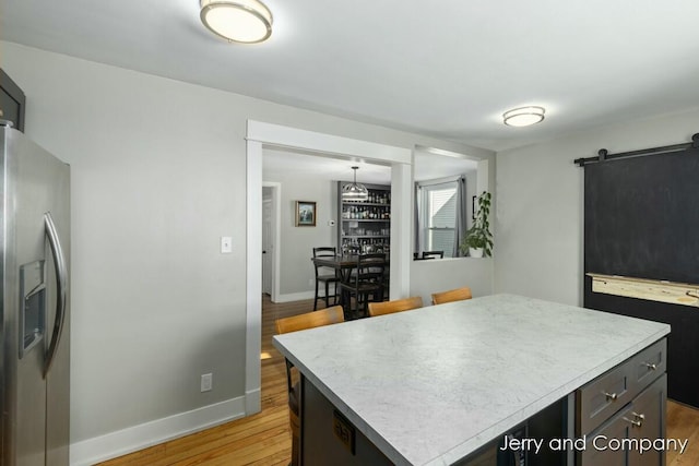 kitchen featuring light wood-type flooring, a center island, a barn door, decorative light fixtures, and stainless steel refrigerator with ice dispenser