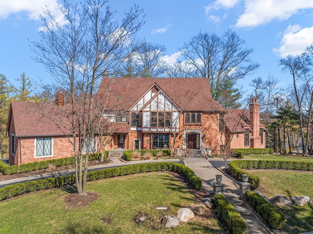 english style home featuring a chimney, a front lawn, and brick siding