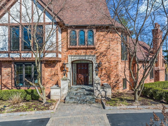 tudor house featuring brick siding and roof with shingles