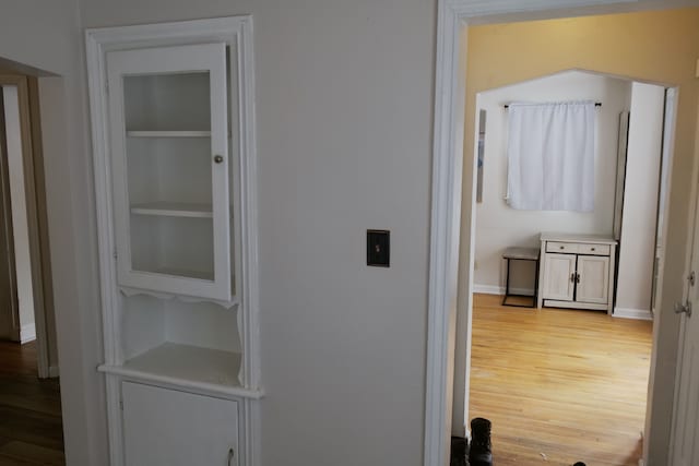 corridor featuring light wood-style floors, built in shelves, and baseboards