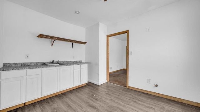 kitchen featuring light hardwood / wood-style flooring, sink, light stone countertops, and white cabinets