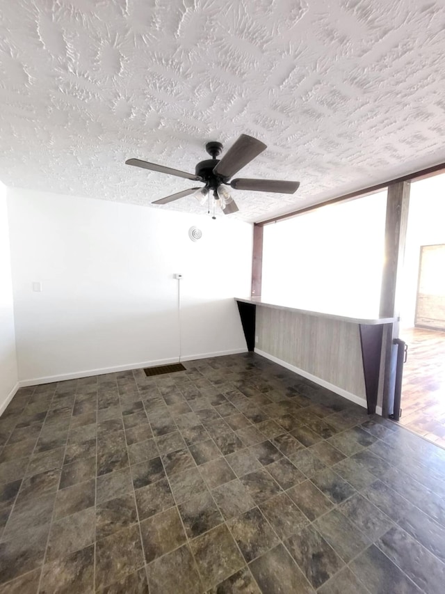 spare room featuring baseboards, a ceiling fan, and a textured ceiling